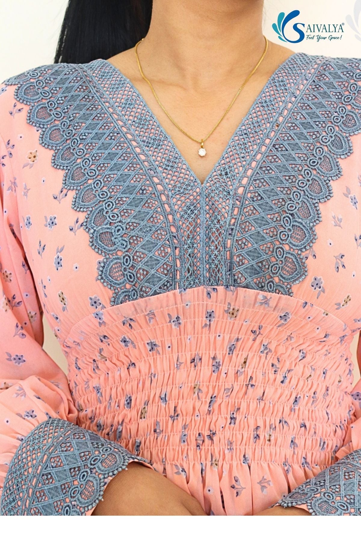 Close-up view of the bodice of the Aashni Smocked Fit & Flare Dress, highlighting the intricate dusty blue geometric lace insert along the V-neckline and matching lace cuffs on the sleeves, set against the light pink georgette fabric with blue micro-floral prints and a detailed smocked elastic waistband.
