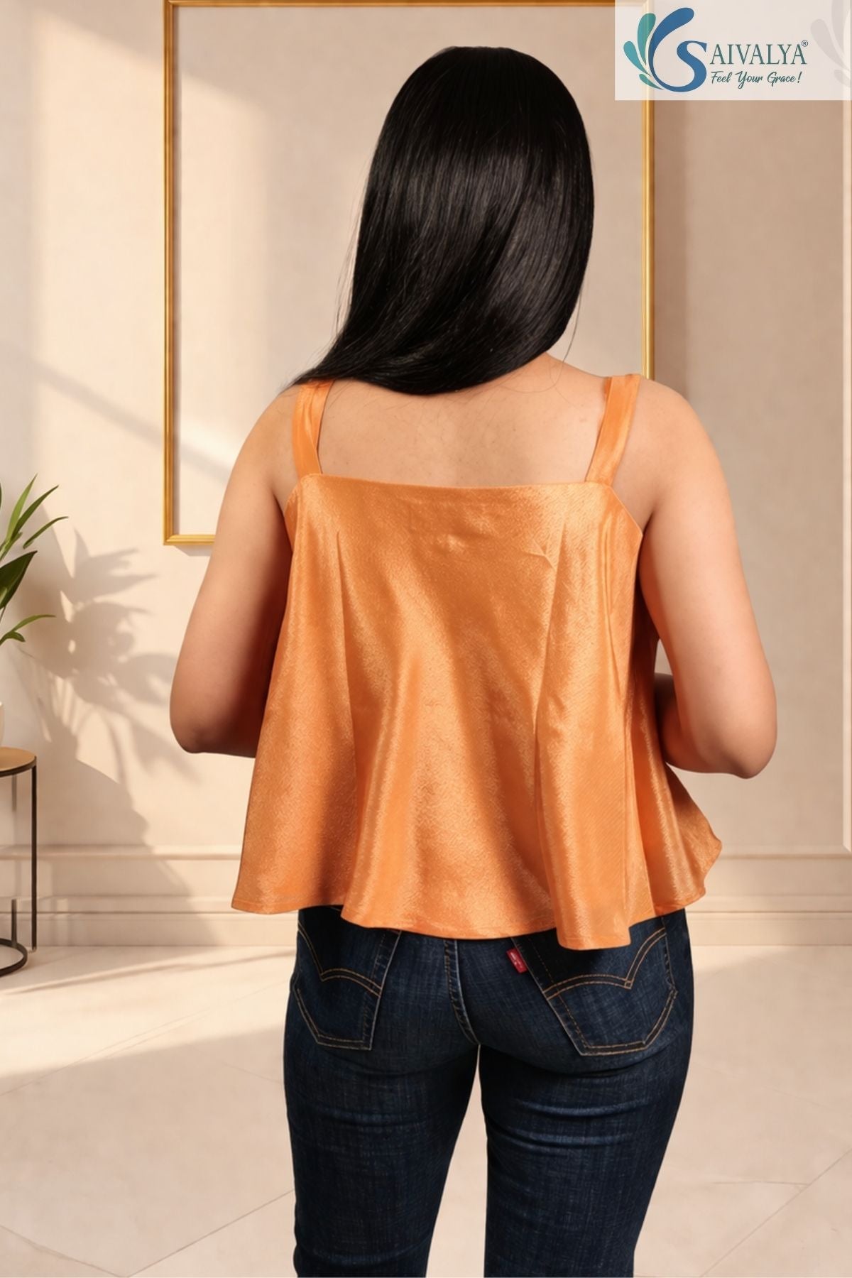 Back view of a woman wearing the Saivalya Ojasvi orange shoulder-tie peplum top with a square back and flared silhouette paired with blue denim jeans