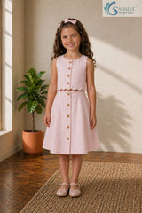 Full-length view of a smiling young girl standing casually, wearing the Blush Petal Cotton Co-ord set featuring a button-down scalloped crop top, matching A-line skirt, and bow flats.