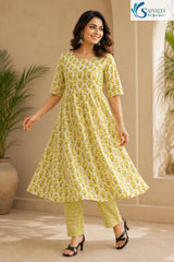 Full-length view of a smiling woman posing dynamically while mid-step, wearing the Citrus Blossom Cotton Kalidar Kurta Set featuring a white and olive-yellow floral print flared anarkali kurta, matching geometric print straight pants, and black low-heeled sandals.
