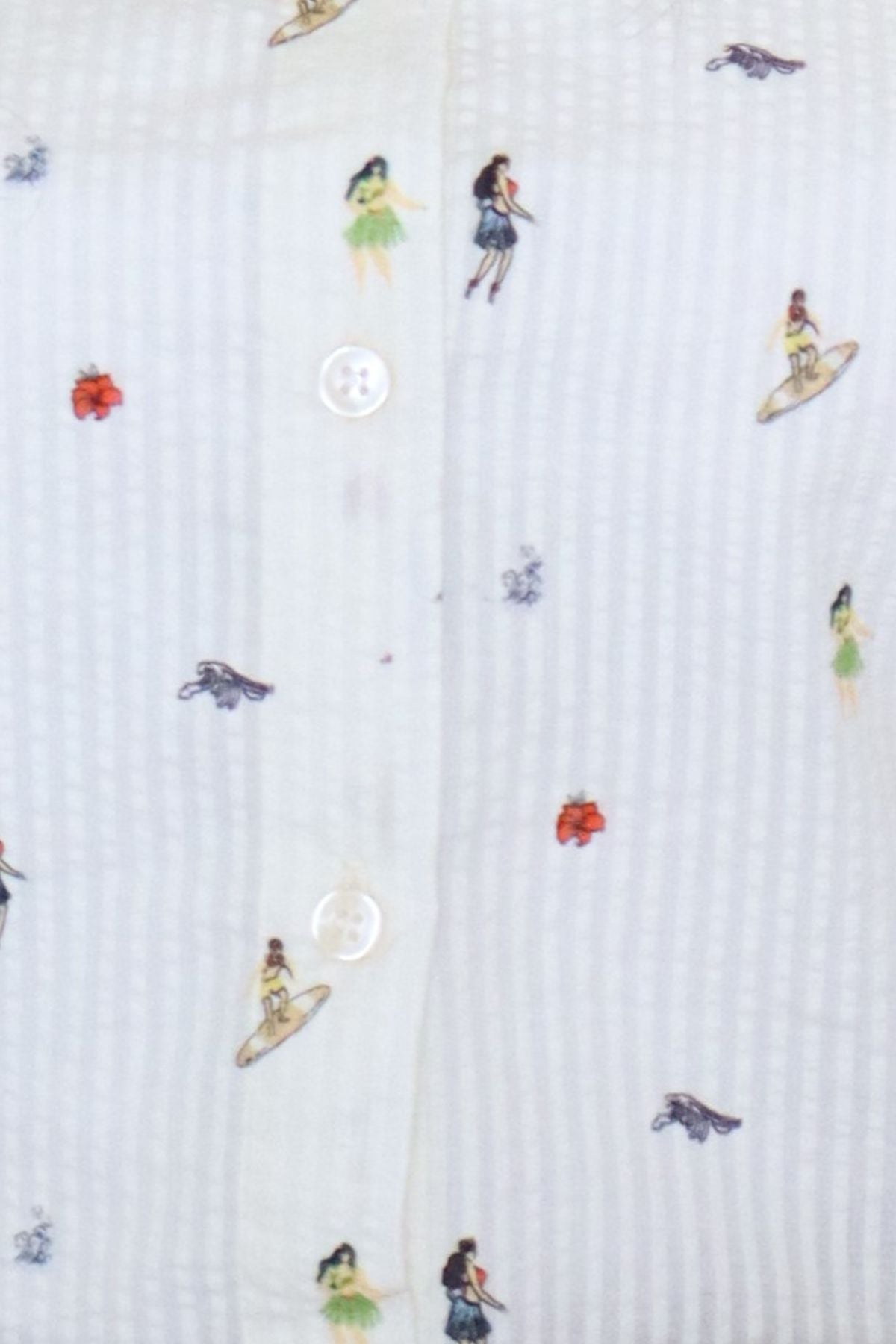Close-up macro view highlighting the white textured seersucker fabric from the Ivory Micro-Print Drawstring Shirt, showcasing the front button placket with white round buttons and scattered colorful miniature graphics of surfers, hula dancers, and tropical flowers.