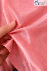 Extreme close-up showing the shimmering fabric texture and fine weave of the Saivalya Nayantara blush pink peplum top held between fingers to demonstrate material quality.