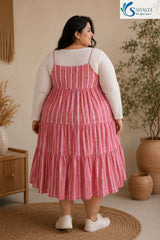 Back view of a woman standing on a round jute rug in a cozy bohemian room, looking over her shoulder, wearing the Raspberry Striped Tiered Midi Dress layered over a ribbed off-white long-sleeve top, highlighting the straight back neckline, thin straps, and pink striped tiered flared skirt, paired with white sneakers.