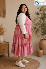 Side view of a smiling woman standing on a round jute rug in a cozy bohemian room, wearing the Raspberry Striped Tiered Midi Dress layered over a ribbed off-white long-sleeve top, highlighting the tiered flared silhouette of the pink striped skirt, paired with white sneakers.