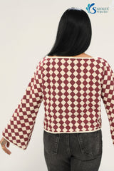 Rear view of the Shatranj Maroon Bell Top, showcasing the continuous maroon and cream harlequin checkered pattern across the back and wide bell sleeves. The top features a clean boat neckline with cream piping, paired with dark charcoal grey jeans.