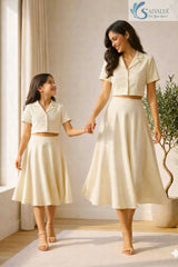 Mother and daughter holding hands and smiling at each other while wearing matching cream Slub Cotton Co-ord sets featuring button-up collared crop shirts and flared midi skirts.