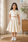 Young girl smiling with her hand in her pocket, wearing a cream Slub Cotton Co-ord set featuring a short-sleeve button-up crop shirt with a notched collar and a matching flared midi skirt.