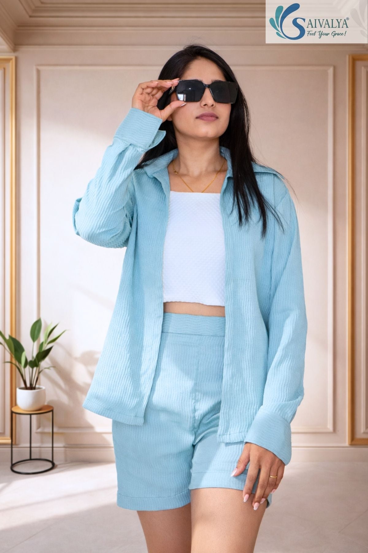 Woman wearing a three-piece powder blue textured shorts set featuring an oversized button-down shirt layered over a white crop top.
