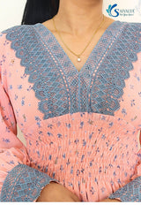 Close-up view of the bodice of the Aashni Smocked Fit & Flare Dress, highlighting the intricate dusty blue geometric lace insert along the V-neckline and matching lace cuffs on the sleeves, set against the light pink georgette fabric with blue micro-floral prints and a detailed smocked elastic waistband.