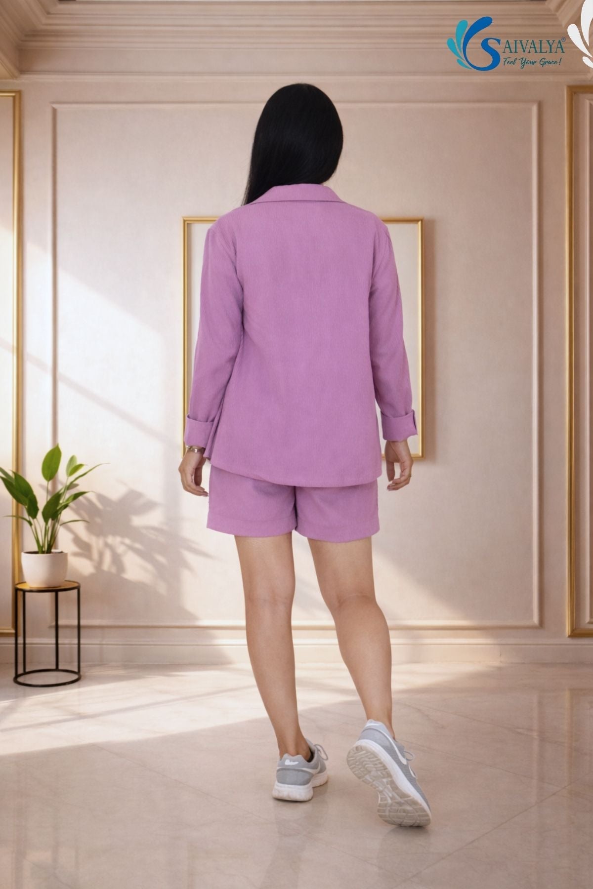 Back view of a woman wearing the Saivalya Amaya mauve textured shorts set featuring an oversized shirt with cuffed sleeves and matching relaxed shorts paired with grey sneakers