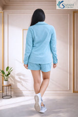 Back view of a woman wearing a light blue textured shorts set featuring a long-sleeve collared shirt and matching lounge shorts.