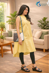 Full-length three-quarter side view of a smiling woman posing in a cozy living room setting with a sofa and plants, wearing the Ira Mustard High-Low Kurta showcasing the asymmetric high-low hemline of the yellow sleeveless button-down kurta, paired with black leggings, black strap sandals, and a blue, grey, and white color-blocked sling bag.